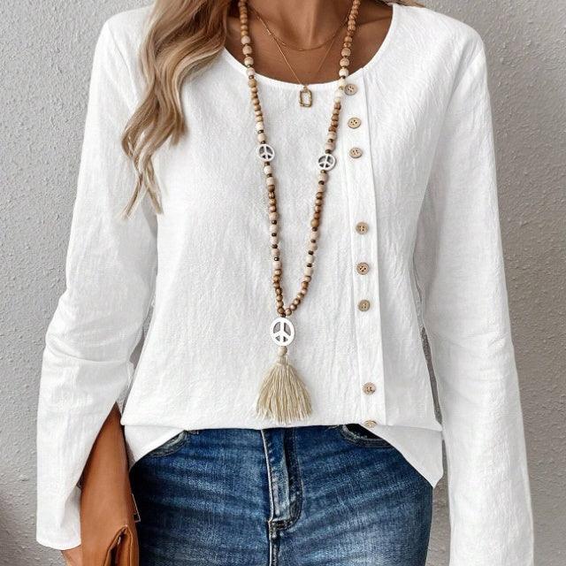 Woman wearing white buttoned blouse with long sleeves and beaded peace sign necklace, paired with blue jeans