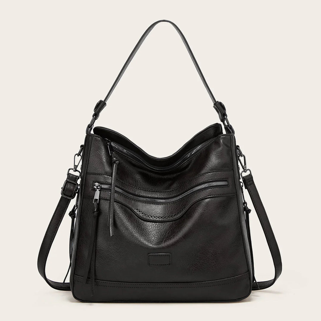 Black leather shoulder bag with front zipper pocket and adjustable strap on beige background