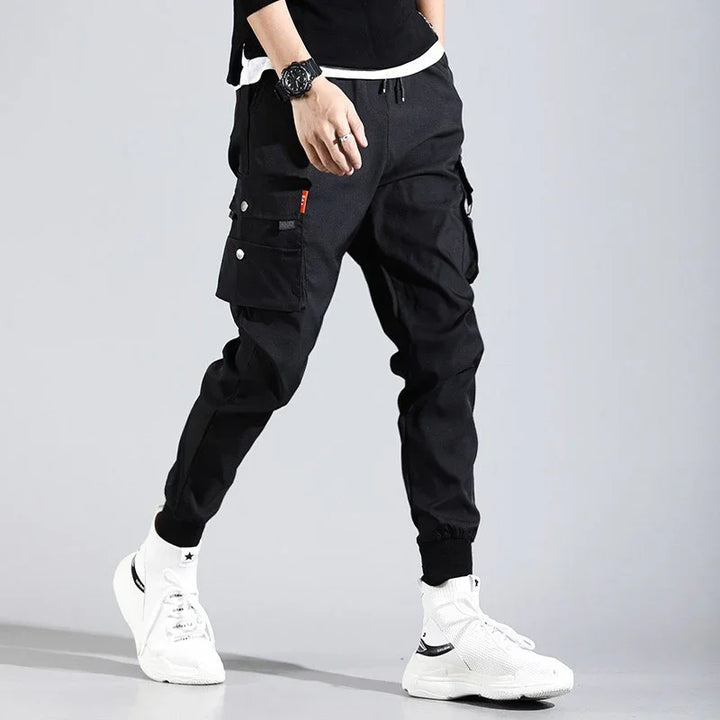 Man wearing black cargo jogger pants with side pockets and white high-top sneakers on gray background