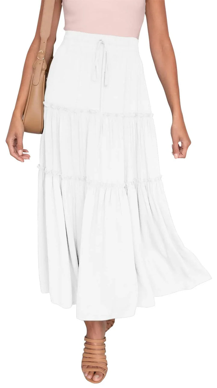 Woman wearing a white tiered maxi skirt with a drawstring waist, paired with tan strappy heels and carrying a tan shoulder bag
