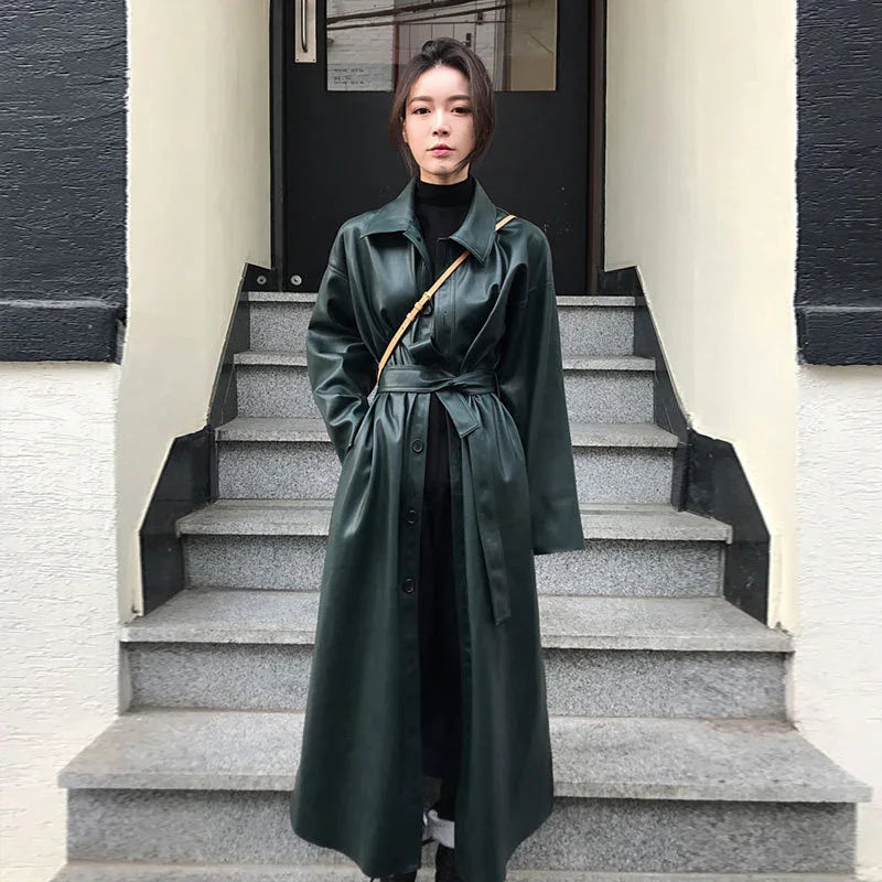 Woman wearing a dark green leather trench coat with a tie belt standing on outdoor stone steps