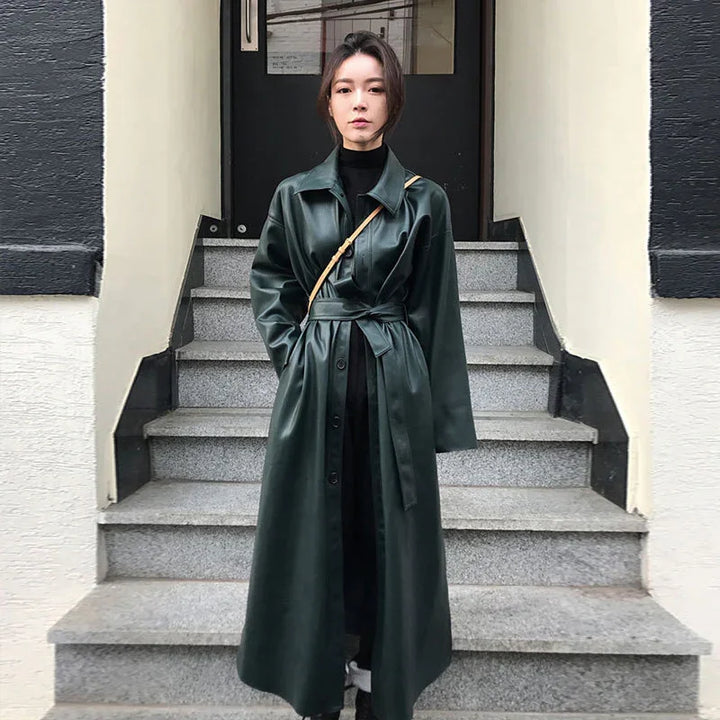 Woman wearing a dark green leather trench coat with a tie belt standing on outdoor stone steps
