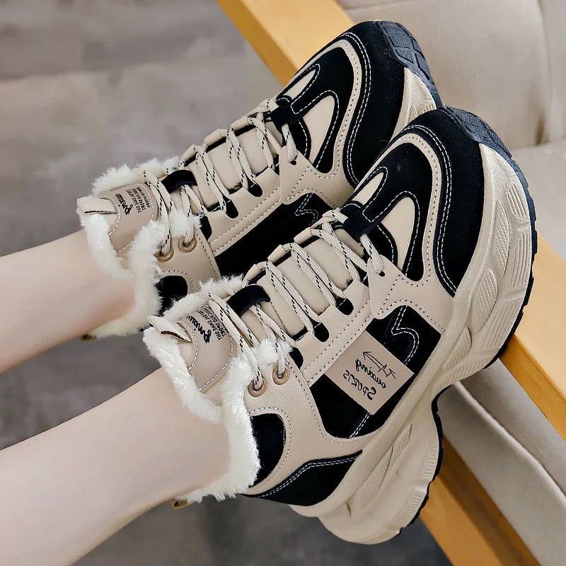 Beige and black fur-lined winter sneakers with thick soles worn by a person sitting on a wooden chair