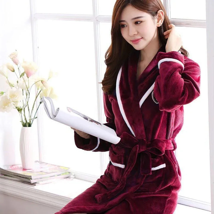Woman sitting by window reading a book wearing plush burgundy robe with white trim