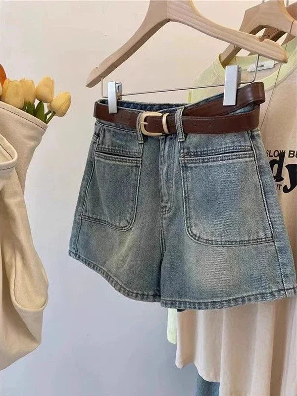 High-waisted light blue denim shorts with front pockets and brown belt hanging on wooden hanger