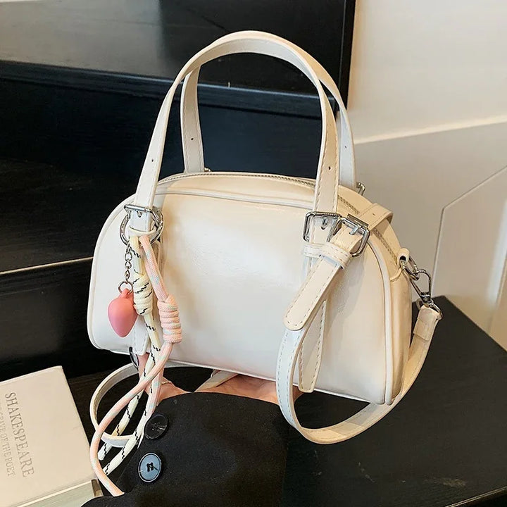 White leather handbag with silver hardware and pink heart keychain held over black surface