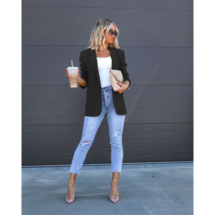 Blonde woman in black blazer, white top, ripped light jeans, clear heels holding coffee and beige clutch