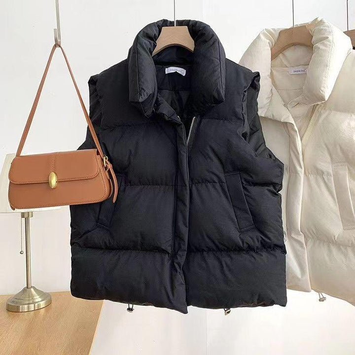 Black and cream puffer vests hanging on wooden hangers with brown leather shoulder bag on lamp stand