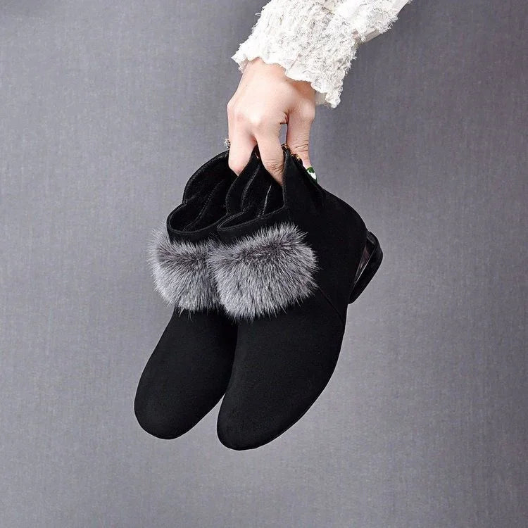 Hand holding black suede ankle boots with gray fur trim against gray background