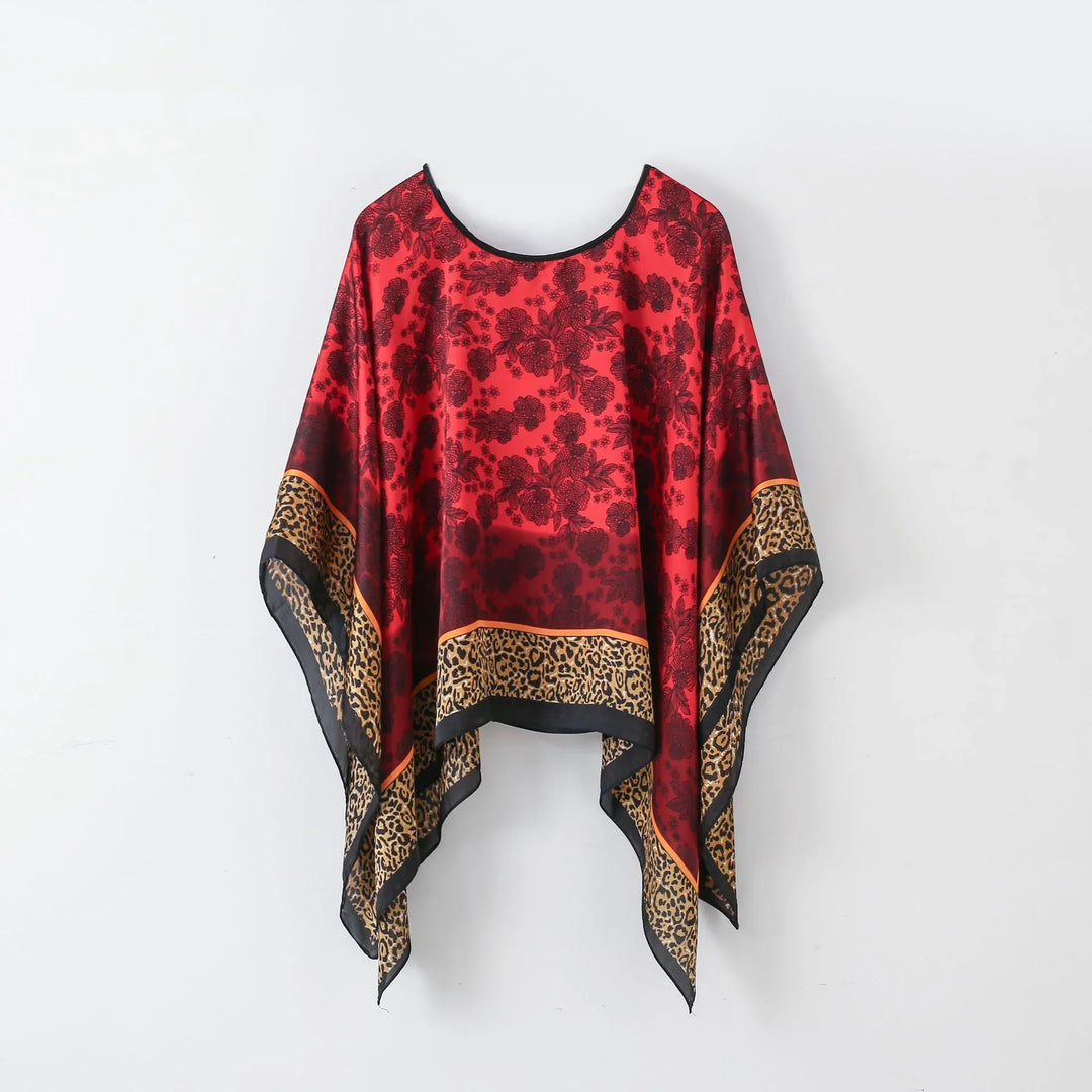 Red and black floral print poncho with leopard print border hanging on white wall