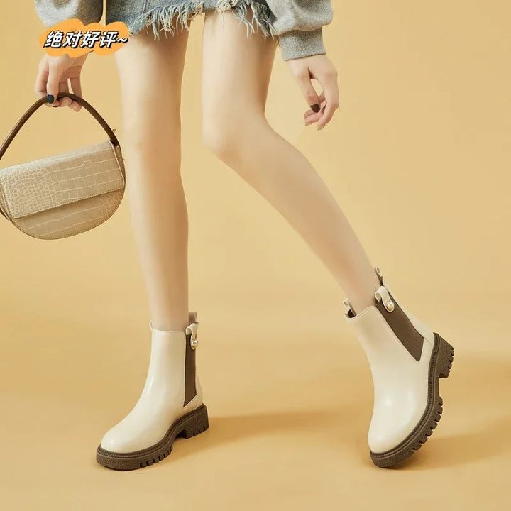 Woman wearing beige ankle boots with chunky black soles and holding a small beige handbag
