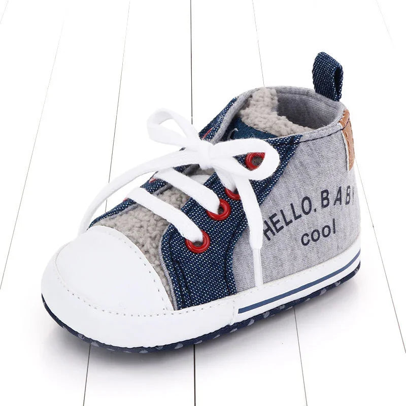 Stylish baby sneaker with white toe, denim accents, gray fabric, and white laces on wooden floor