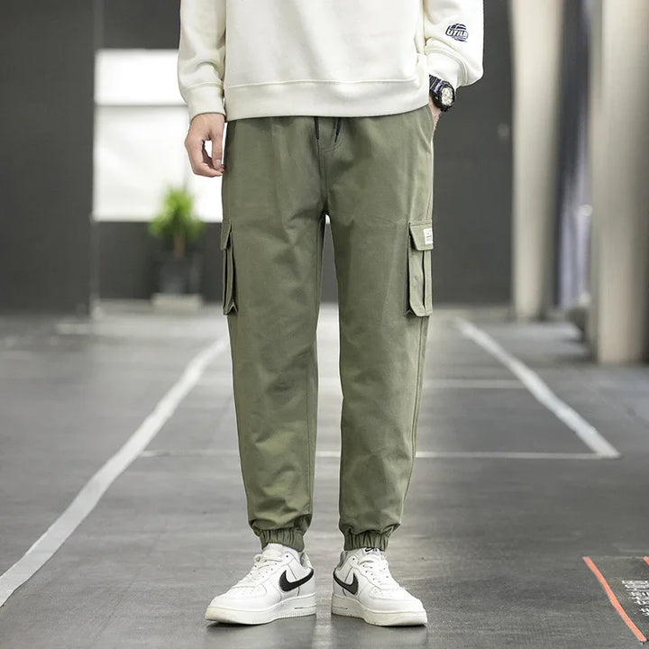 Person wearing olive green cargo jogger pants and white Nike sneakers in an urban setting