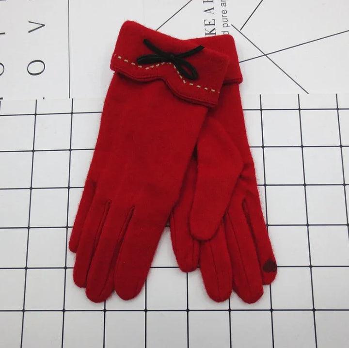 Pair of red winter gloves with black bow and beige stitching on grid background