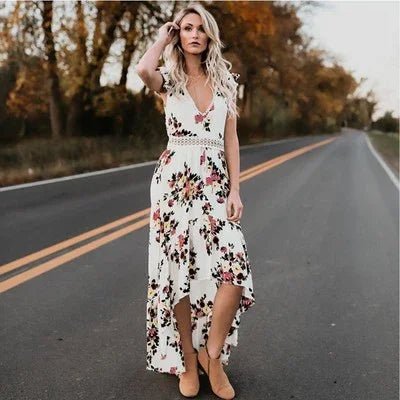 Blonde woman in white floral high-low dress standing on empty road with fall trees background
