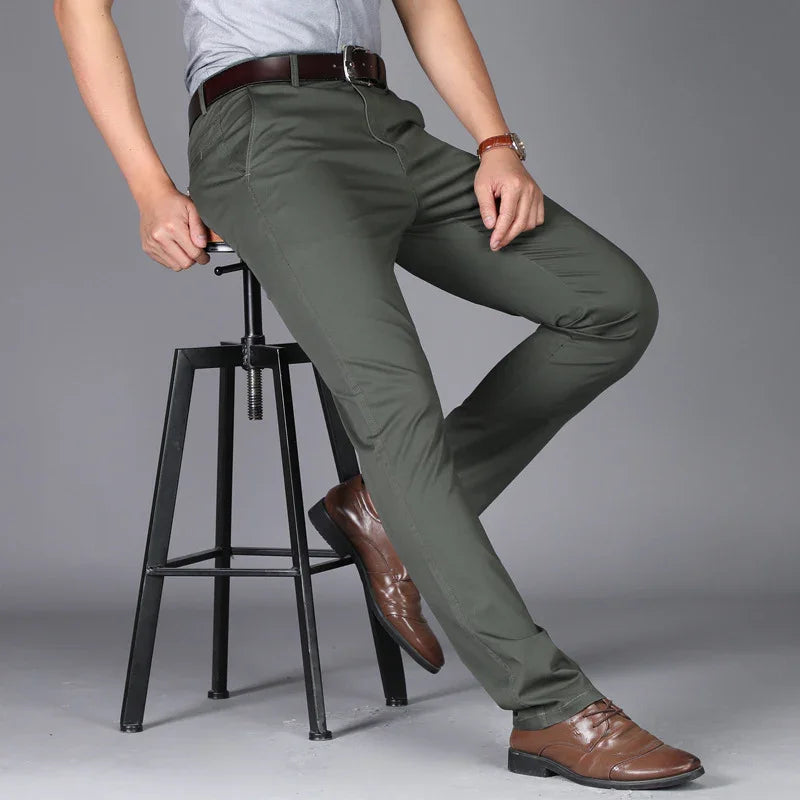 Man wearing olive green slim fit pants with brown leather belt and shoes, sitting on a black metal stool