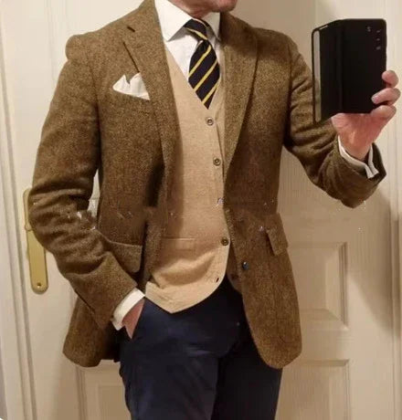 Man wearing brown tweed blazer, beige cardigan, white shirt, striped tie, and navy pants taking a mirror selfie