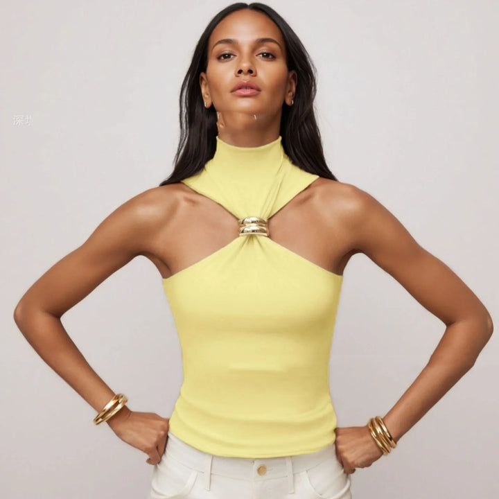 Woman wearing yellow sleeveless halter top with gold ring detail, white pants, and gold bracelets