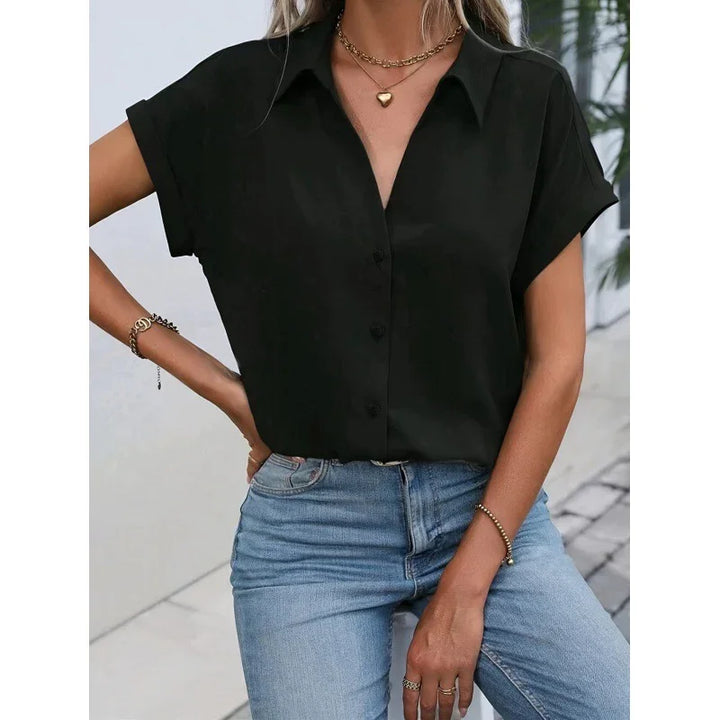 Woman wearing black short-sleeve collared button-up blouse paired with light blue jeans and gold accessories