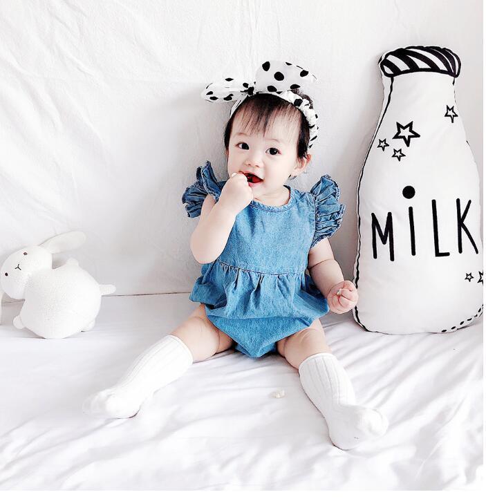 Cute baby girl in denim dress and polka dot headband sitting with milk bottle pillow and white bunny toy