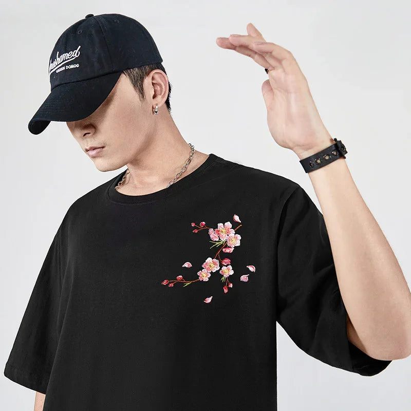 Man wearing black t-shirt with pink flower embroidery and black cap against white background