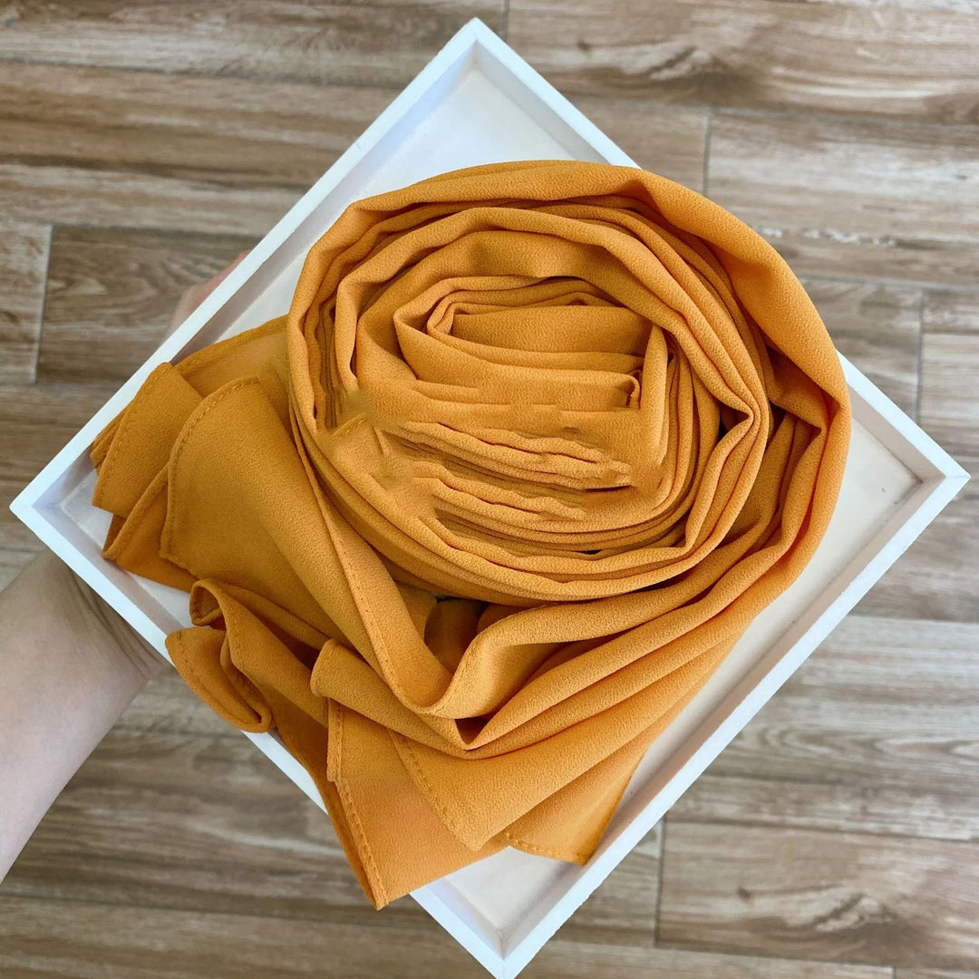 Hand holding a white tray with a neatly rolled orange fabric scarf on wooden floor