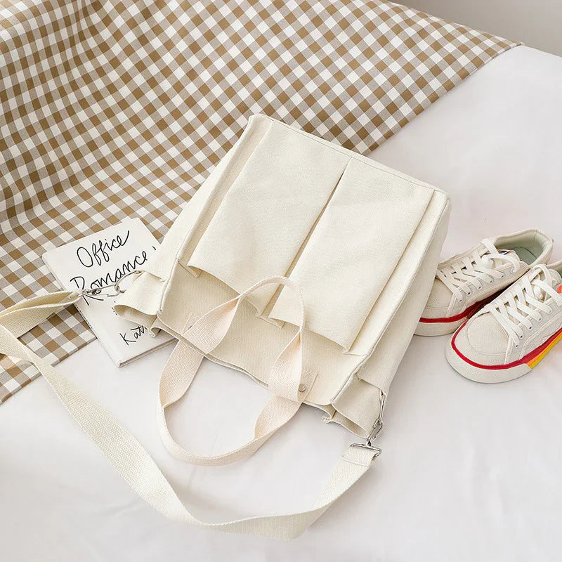 Cream canvas tote bag with dual straps, placed on white surface near sneakers and checkered cloth