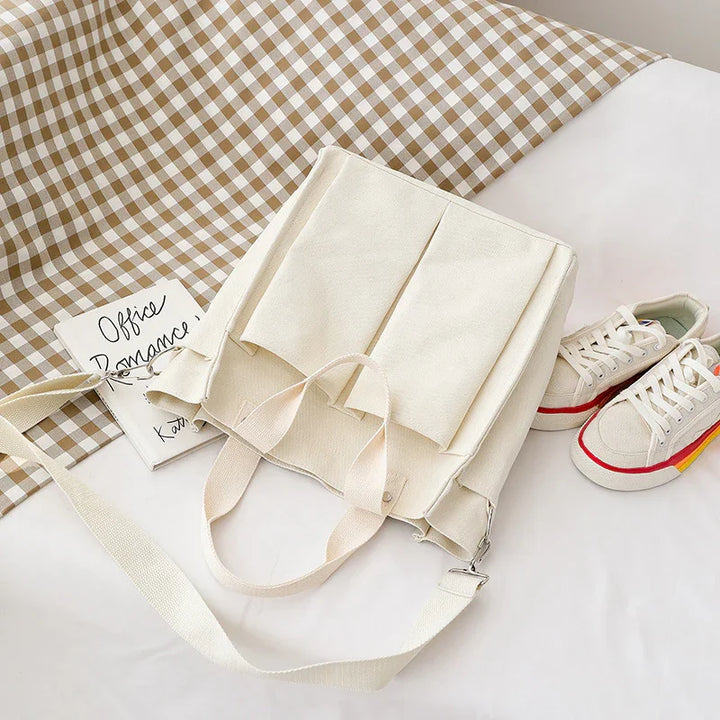 Cream canvas tote bag with dual straps, placed on white surface near sneakers and checkered cloth