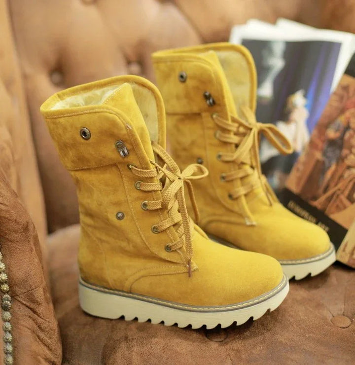 Yellow suede lace-up winter boots with white rugged soles on a brown tufted sofa