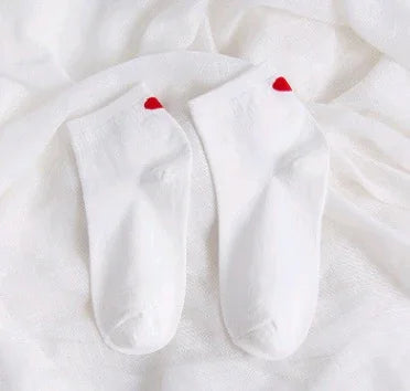 Pair of white ankle socks with red heart detail on heels laid on white fabric