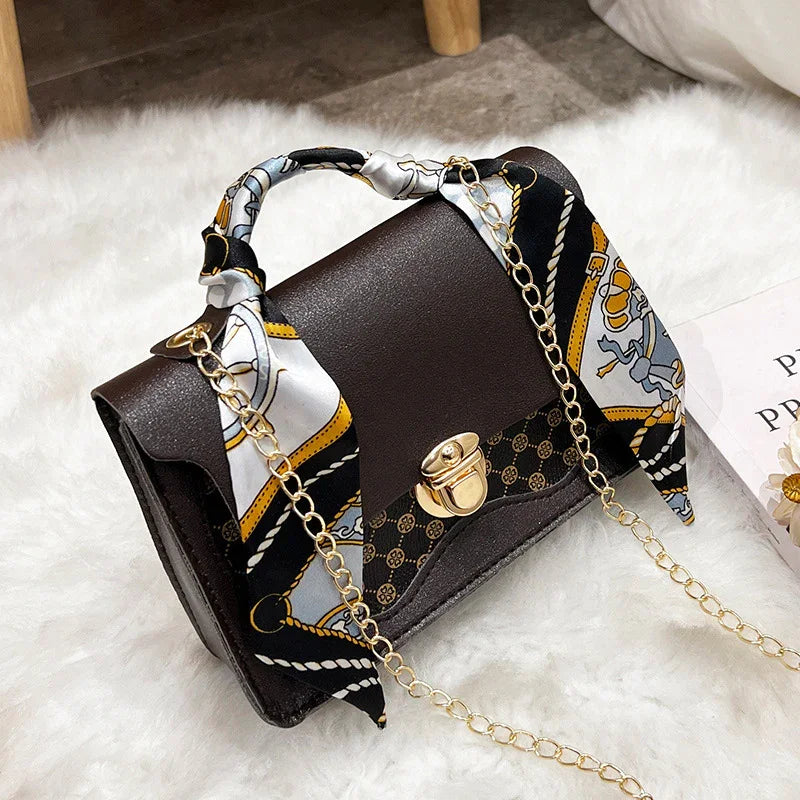 Elegant dark brown leather handbag with gold clasp, chain strap, and silk scarf handle on white fur