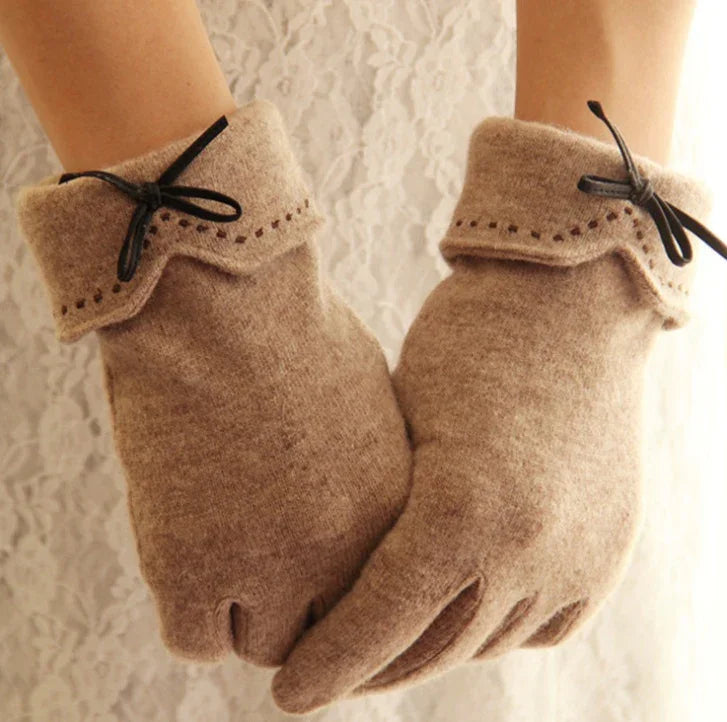 Pair of beige wool gloves with black ribbon bow and decorative stitching on cuffs