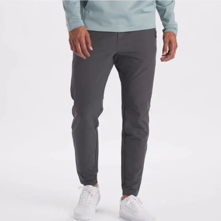Men's slim-fit dark gray casual pants paired with white sneakers on a white background