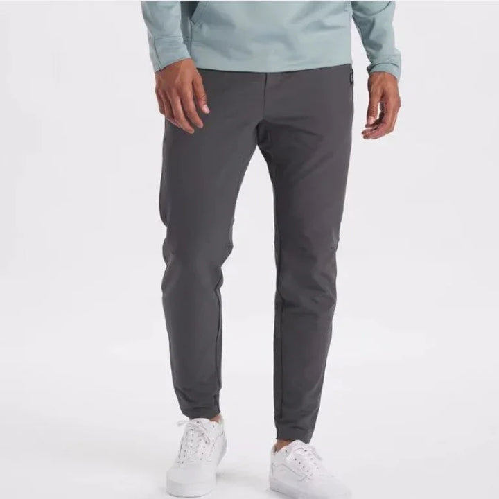 Men's slim-fit dark gray casual pants paired with white sneakers on a white background