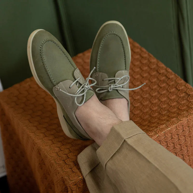 Casual olive green suede lace-up shoes worn with beige pants, resting on textured brown surface