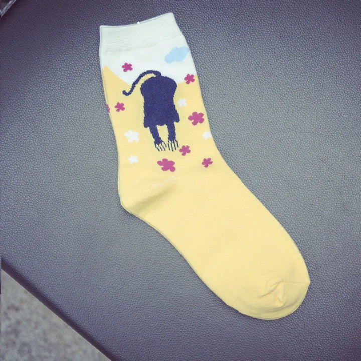 Yellow sock with black cat silhouette, pink and white flowers, and blue cloud pattern on textured surface