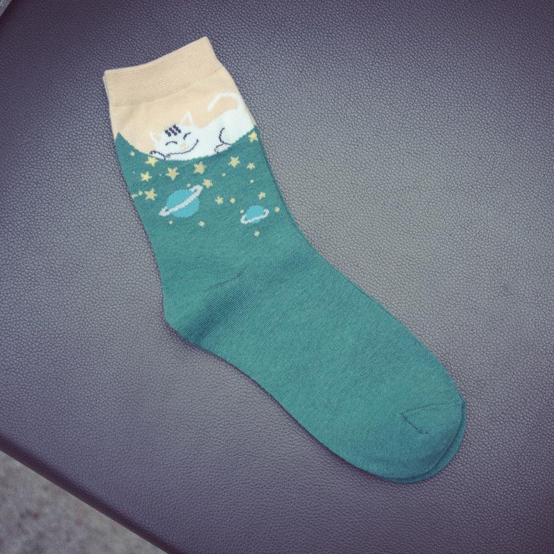 Green sock with beige cuff featuring a white cat and planet and star designs on textured surface