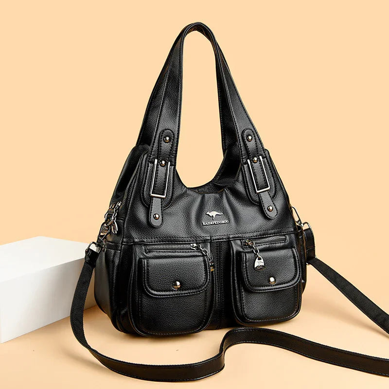 Black leather handbag with dual front pockets, silver buckles, and adjustable shoulder strap on beige background