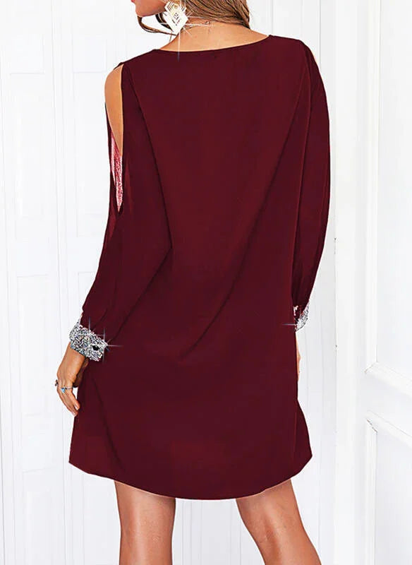 Woman wearing a burgundy long-sleeve dress with silver sequined cuffs and shoulder cutouts
