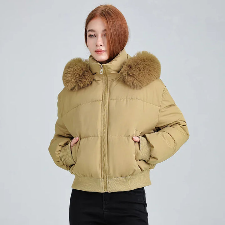 Woman wearing beige puffer jacket with large fur collar and black pants on gray background
