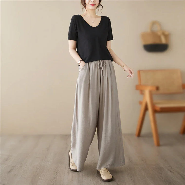 Woman wearing black short-sleeve top and loose grey wide-leg pants in modern indoor setting