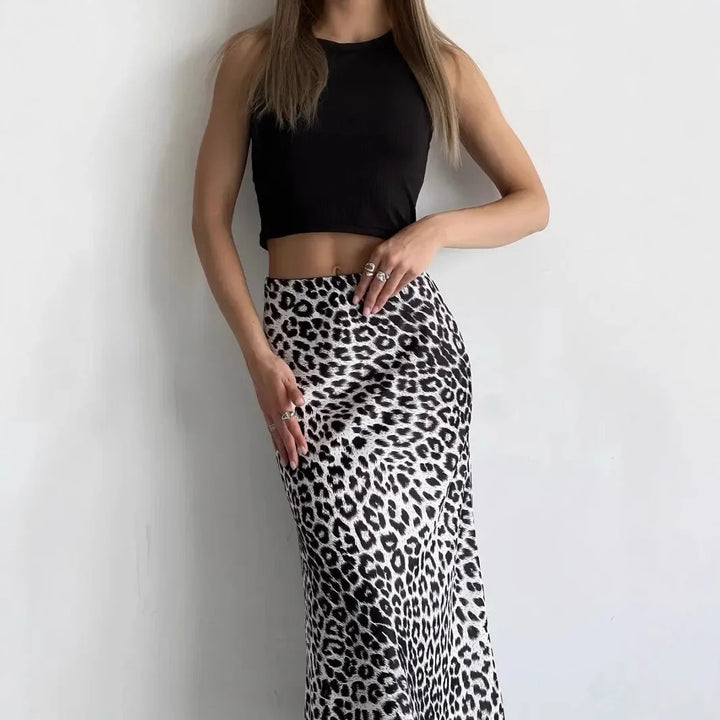 Woman wearing black crop top and high-waisted black and white leopard print skirt against white wall