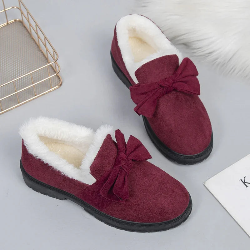 Burgundy women's slip-on slippers with fluffy white lining and decorative bows on a gray surface