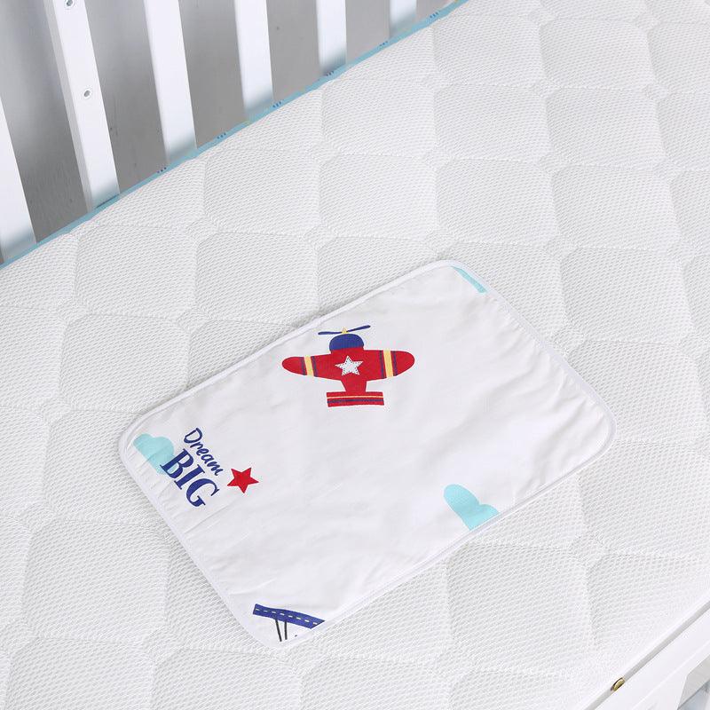 White crib mattress with quilted pattern and a baby cloth featuring a red airplane and 'Dream Big' text