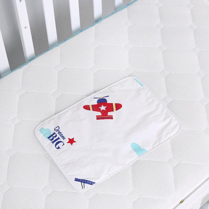 White crib mattress with quilted pattern and a baby cloth featuring a red airplane and 'Dream Big' text