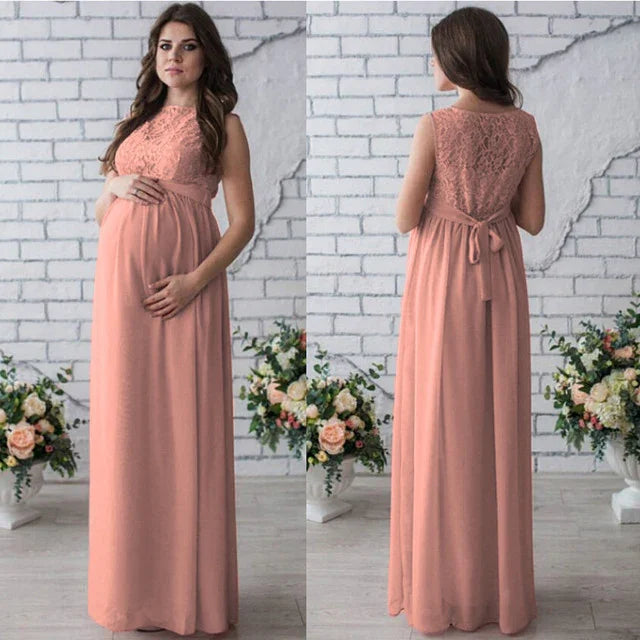 Pregnant woman wearing sleeveless blush pink lace maternity dress posing indoors with floral arrangements