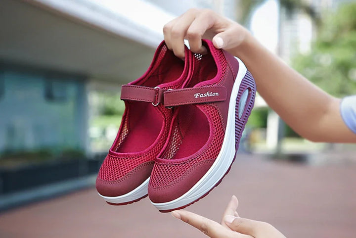 Person holding red mesh breathable casual shoes with white sole and adjustable strap outdoors