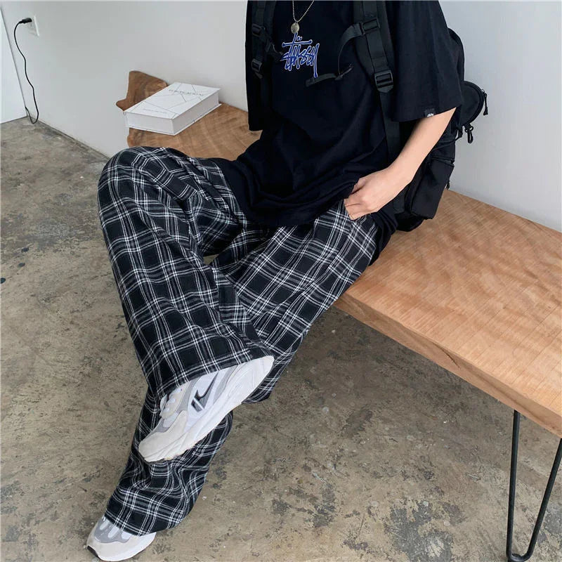 Person wearing black graphic t-shirt, black and white plaid pants, white sneakers sitting on wooden bench