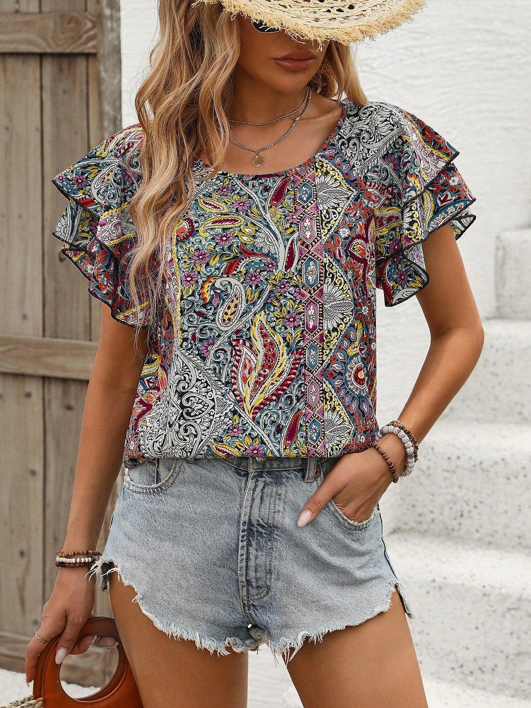Woman wearing colorful paisley print short-sleeve blouse with ruffle sleeves and distressed denim shorts