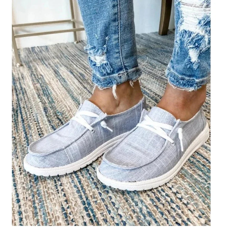 Close-up of feet wearing casual light gray fabric slip-on shoes with white laces on a woven rug